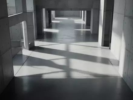 Ein minimalistischer, leerer Flur mit geometrischen Schatten auf einem Betonboden, der eine kühle, sachliche Atmosphäre erzeugt. - Foto: über boerse-global.de