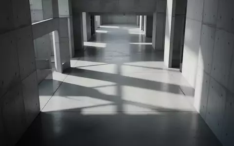Ein minimalistischer, leerer Flur mit geometrischen Schatten auf einem Betonboden, der eine kühle, sachliche Atmosphäre erzeugt. - Foto: über boerse-global.de