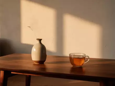 Ein minimalistischer Wohnraum mit einem Holztisch, einer Vase und einer Tasse Tee im warmen Licht der goldenen Stunde. - Foto: über boerse-global.de