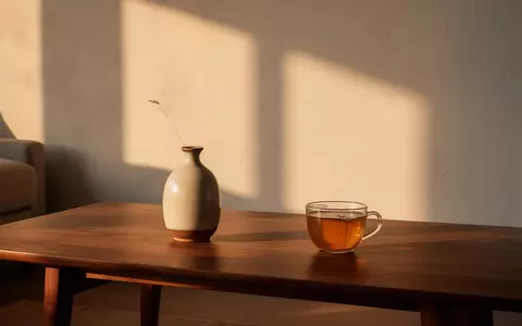 Ein minimalistischer Wohnraum mit einem Holztisch, einer Vase und einer Tasse Tee im warmen Licht der goldenen Stunde. - Foto: über boerse-global.de