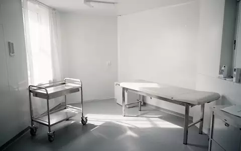 Ein minimalistischer, leerer Behandlungsraum in einer Arztpraxis mit einem Edelstahltrolley und einer Untersuchungsliege bei natürlichem Tageslicht. - Foto: über boerse-global.de