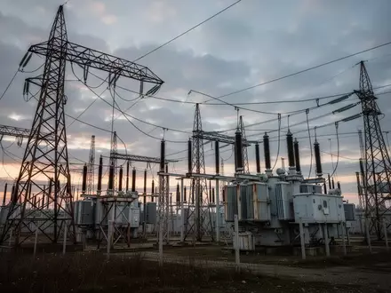 Hochspannungsmasten einer Stromtrasse in einer industriellen Landschaft bei Dämmerung. - Foto: über boerse-global.de