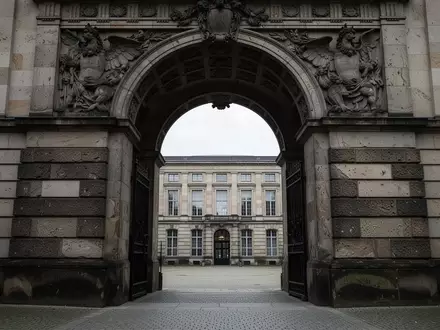 Ein schwerer, steinerner Torbogen führt in einen ruhigen, schattigen Innenhof eines Berliner Regierungsgebäudes. - Foto: über boerse-global.de
