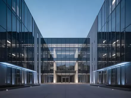 Modernes Verwaltungsgebäude bei Dämmerung mit geometrischer Glasfassade. - Foto: über boerse-global.de