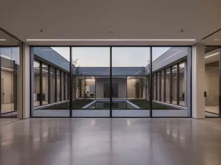 Ein minimalistisch gestalteter, leerer Büroraum mit großen Glasfronten und Blick in einen ruhigen Innenhof bei Dämmerung. - Foto: über boerse-global.de