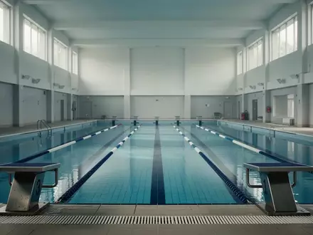Ein leeres Hallenbad mit blauen Kacheln und Startblöcken in einer minimalistischen Architektur. - Foto: über boerse-global.de