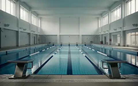 Ein leeres Hallenbad mit blauen Kacheln und Startblöcken in einer minimalistischen Architektur. - Foto: über boerse-global.de
