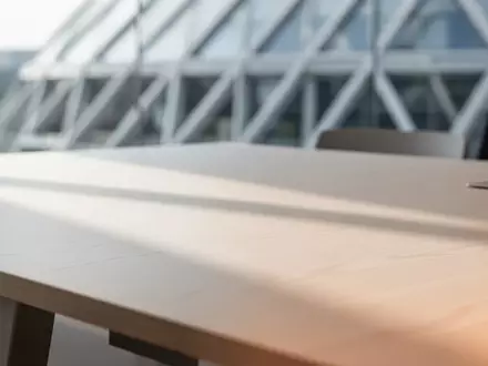 Ein minimalistischer Arbeitsplatz mit einer leeren Holzoberfläche und unscharfer, moderner Architektur im Hintergrund. - Foto: über boerse-global.de