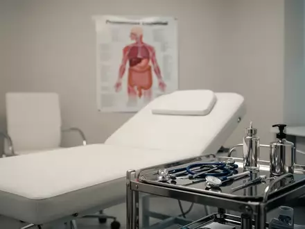 Ein minimalistisch eingerichtetes, helles Arztzimmer mit medizinischen Instrumenten und einem anatomischen Schaubild. - Foto: über boerse-global.de