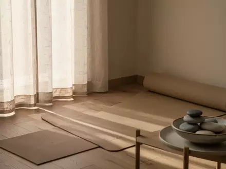 Ein minimalistisch eingerichteter Wellness-Raum mit weichem Tageslicht, einer Yogamatte und einer Schale mit Kieselsteinen. - Foto: über boerse-global.de