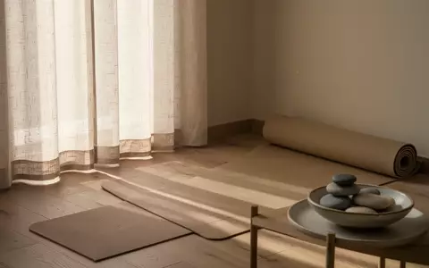 Ein minimalistisch eingerichteter Wellness-Raum mit weichem Tageslicht, einer Yogamatte und einer Schale mit Kieselsteinen. - Foto: über boerse-global.de
