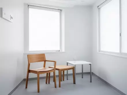 Ein minimalistischer, heller Behandlungsraum mit einem leeren Stuhl und einem Glas Wasser auf einem Beistelltisch. - Foto: über boerse-global.de
