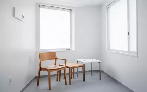 Ein minimalistischer, heller Behandlungsraum mit einem leeren Stuhl und einem Glas Wasser auf einem Beistelltisch. - Foto: über boerse-global.de