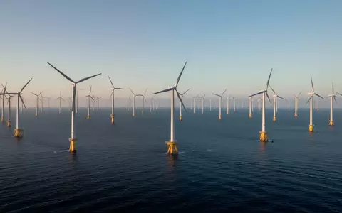 Ein moderner Offshore-Windpark vor einer ruhigen Meeresküste bei Sonnenaufgang. - Foto: über boerse-global.de
