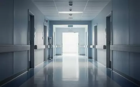 Ein klinisch sauberer, menschenleerer Krankenhausflur in modernem Design mit sanfter Beleuchtung und reflektierenden Bodenflächen. - Foto: über boerse-global.de