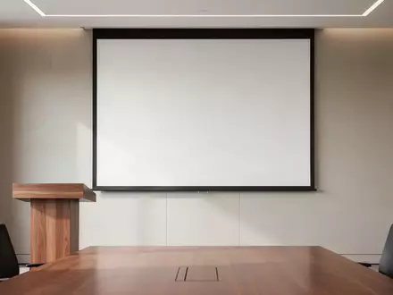 Ein minimalistischer Konferenzraum mit einem leeren Rednerpult vor einer unbeschriebenen, weißen Projektionsfläche. - Foto: über boerse-global.de
