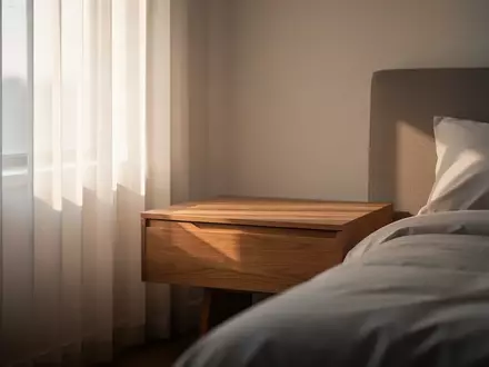 Ein minimalistisch eingerichtetes Schlafzimmer am frühen Morgen mit sanftem Tageslicht, das durch einen Vorhang fällt. - Foto: über boerse-global.de