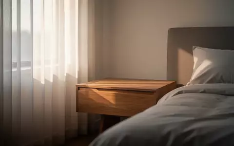 Ein minimalistisch eingerichtetes Schlafzimmer am frühen Morgen mit sanftem Tageslicht, das durch einen Vorhang fällt. - Foto: über boerse-global.de