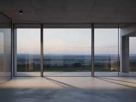 Ein minimalistischer, moderner Innenraum mit großen Glasfronten und Blick auf eine weite Landschaft in der Abenddämmerung. - Foto: über boerse-global.de