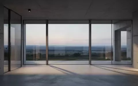 Ein minimalistischer, moderner Innenraum mit großen Glasfronten und Blick auf eine weite Landschaft in der Abenddämmerung. - Foto: über boerse-global.de