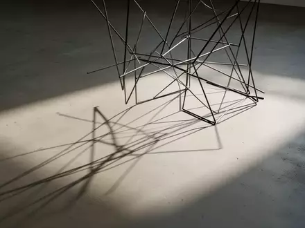 Ein minimalistisches Drahtgestell wirft einen scharfen Schatten auf einen schlichten Betonboden. - Foto: über boerse-global.de