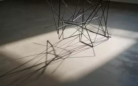 Ein minimalistisches Drahtgestell wirft einen scharfen Schatten auf einen schlichten Betonboden. - Foto: über boerse-global.de