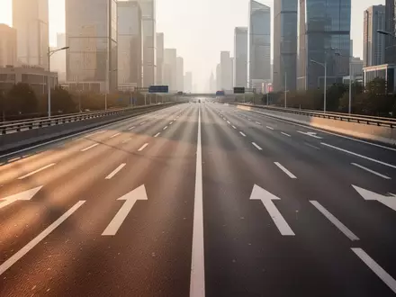 Eine leere, moderne Stadtschnellstraße mit klarer Fahrbahnmarkierung bei Sonnenuntergang vor einer urbanen Skyline. - Foto: über boerse-global.de