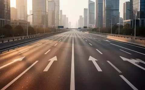 Eine leere, moderne Stadtschnellstraße mit klarer Fahrbahnmarkierung bei Sonnenuntergang vor einer urbanen Skyline. - Foto: über boerse-global.de