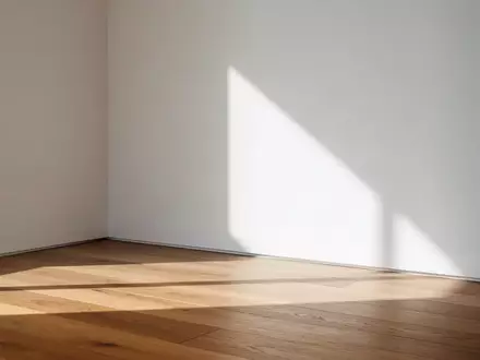 Ein minimalistischer, sonnendurchfluteter Raum mit einer leeren weißen Wand und einem Holzboden. - Foto: über boerse-global.de