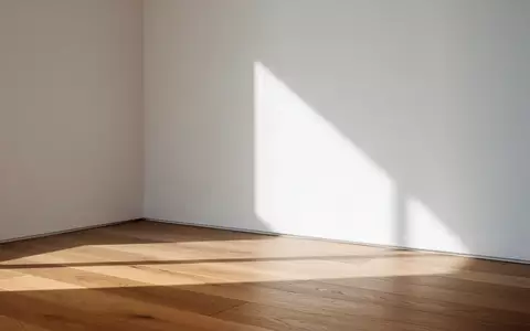 Ein minimalistischer, sonnendurchfluteter Raum mit einer leeren weißen Wand und einem Holzboden. - Foto: über boerse-global.de