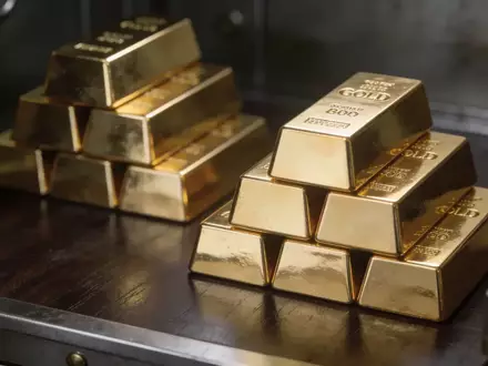 Mehrere gestapelte Goldbarren auf einer dunklen Holzoberfläche in einem Tresorraum. - Foto: über boerse-global.de
