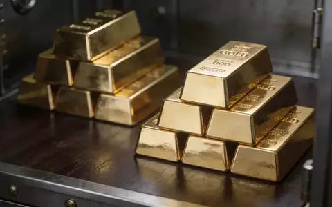 Mehrere gestapelte Goldbarren auf einer dunklen Holzoberfläche in einem Tresorraum. - Foto: über boerse-global.de