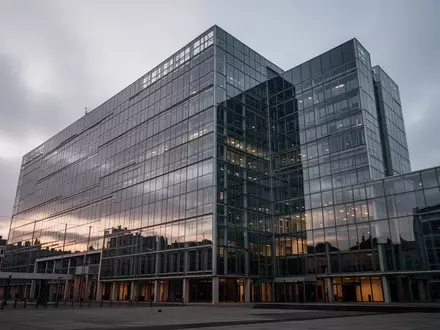 Die Glasfassade des Berlaymont-Gebäudes in Brüssel bei Dämmerung unter einem bewölkten Himmel. - Foto: über boerse-global.de