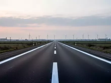 Eine leere, asphaltierte Straße in einer flachen Industrielandschaft bei Dämmerung mit weißen Fahrbahnmarkierungen. - Foto: über boerse-global.de