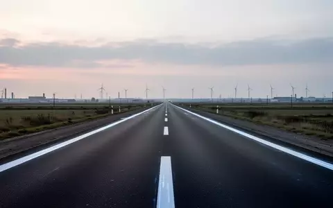 Eine leere, asphaltierte Straße in einer flachen Industrielandschaft bei Dämmerung mit weißen Fahrbahnmarkierungen. - Foto: über boerse-global.de