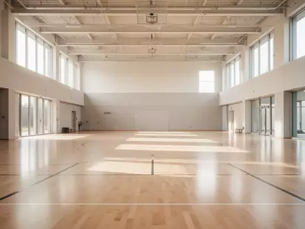 Helle, moderne Sporthalle mit hellem Holzboden und großen Fenstern ohne Personen. - Foto: über boerse-global.de