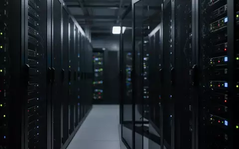 Dunkler, moderner Serverraum mit fokussierten Metall-Serverracks und verschwommenen Statuslichtern im Hintergrund. - Foto: über boerse-global.de