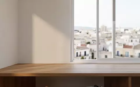 Ein minimalistischer, heller Arbeitsplatz mit Holztisch vor einem Fenster mit Blick auf eine mediterrane Stadt. - Foto: über boerse-global.de