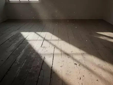 Ein leerer, sonnendurchfluteter Raum mit langen Schatten auf einem hölzernen Boden, der eine Atmosphäre der Stille vermittelt. - Foto: über boerse-global.de