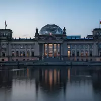 Das Berliner Reichstagsgebäude in der Abenddämmerung bei blauem Licht mit Spiegelung im Wasser der Spree. - Foto: über boerse-global.de