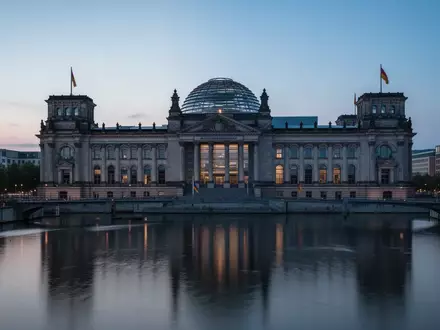 Das Berliner Reichstagsgebäude in der Abenddämmerung bei blauem Licht mit Spiegelung im Wasser der Spree. - Foto: über boerse-global.de