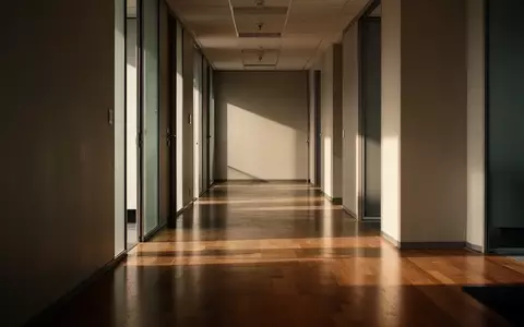 Ein leerer, sonnendurchfluteter Büroflur mit langen Schatten auf dem Boden, der eine Atmosphäre der Stille vermittelt. - Foto: über boerse-global.de