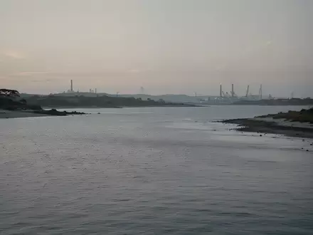 Die Küstenlandschaft der Jadebucht bei Dämmerung mit ruhigem Wasser und einer fernen Industriekulisse am Horizont. - Foto: über boerse-global.de
