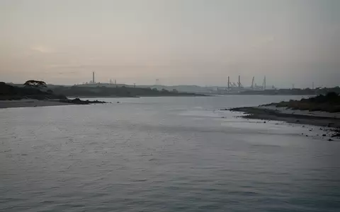 Die Küstenlandschaft der Jadebucht bei Dämmerung mit ruhigem Wasser und einer fernen Industriekulisse am Horizont. - Foto: über boerse-global.de