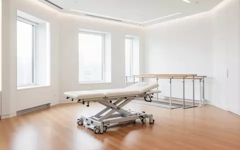 Ein heller, moderner Therapieraum in einer Klinik mit einer leeren Behandlungsliege und einem Barren zur Gangschulung. - Foto: über boerse-global.de