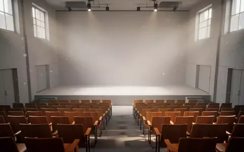 Ein minimalistischer, leerer Hörsaal mit Reihen aus Holzstühlen und hellem, natürlichem Tageslicht, das auf die Bühne fällt. - Foto: über boerse-global.de