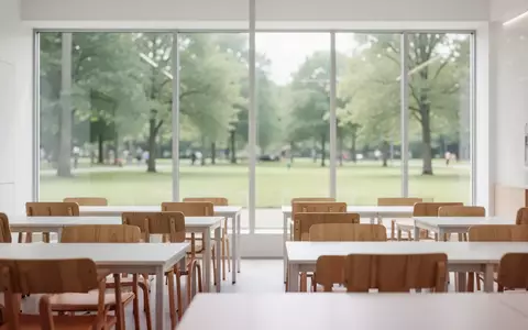Ein heller, leerer Unterrichtsraum mit modernen Möbeln und großen Fenstern mit Blick ins Grüne. - Foto: über boerse-global.de