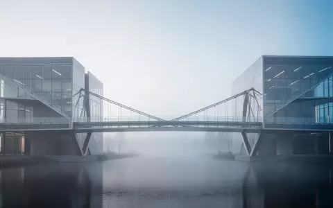 Eine moderne, minimalistische Brücke aus Glas und Stahl, die zwei architektonische Strukturen in einer nebligen Umgebung verbindet. - Foto: über boerse-global.de