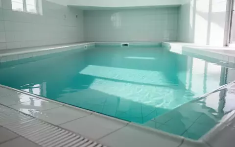 Ein leeres, hell beleuchtetes Schwimmbecken mit klarem türkisfarbenem Wasser in einer minimalistischen Umgebung. - Foto: über boerse-global.de
