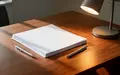 Ein minimalistischer Schreibtisch mit Papierstapel und Schreibtischlampe in einem hellen, modernen Büro. - Foto: über boerse-global.de